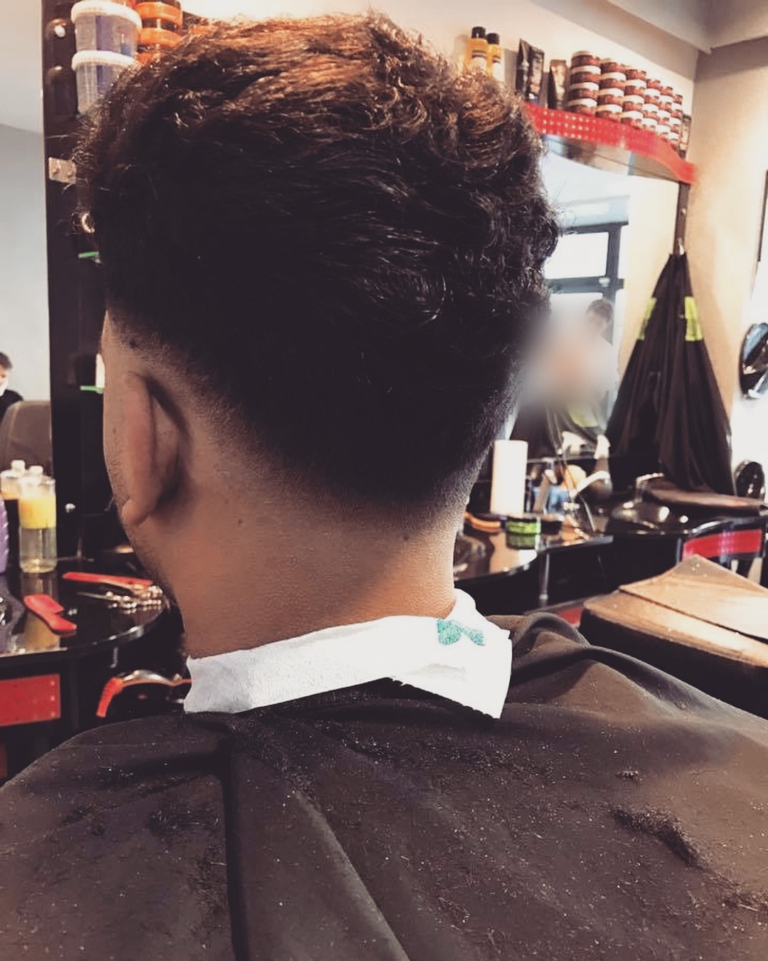 Klant van achteren na een fade, met de kapmantel om en de zaak op de achtergrond